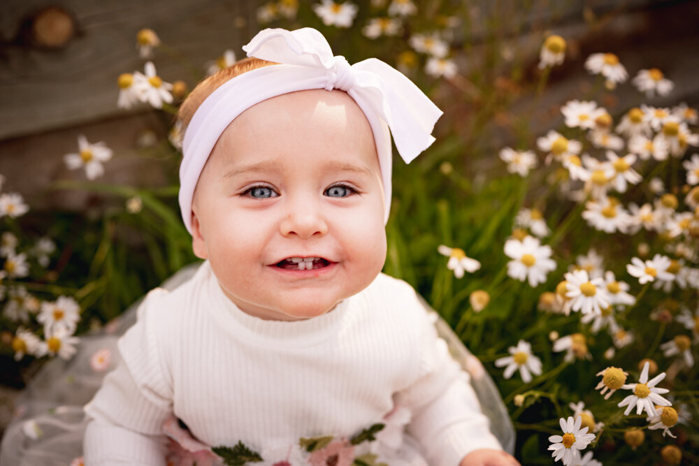a baby with two front teeth smiles in a field of daisys