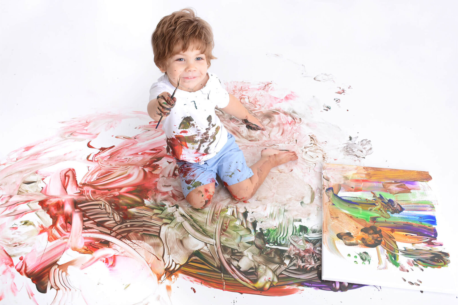 boy smiles while the floor is covered in paint at his photoshoot