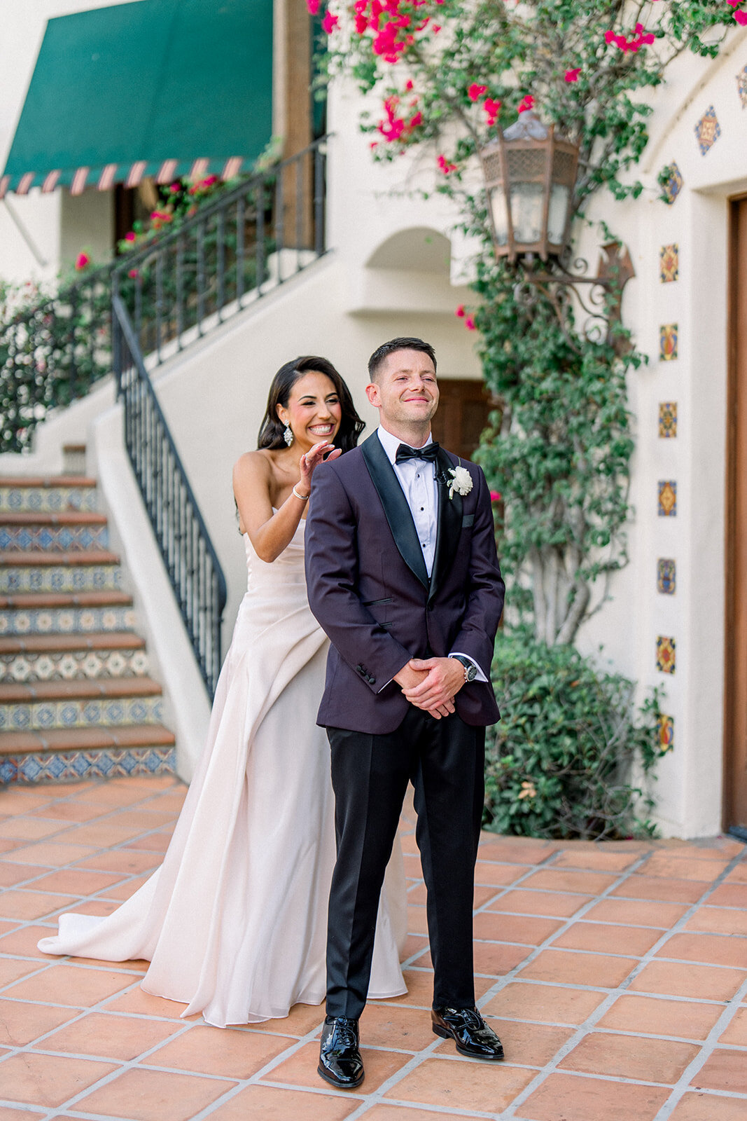 Bride and groom pose beneath green awning and florals on the Spanish-style steps at Hummingbird Nest Ranch in Los Angeles.