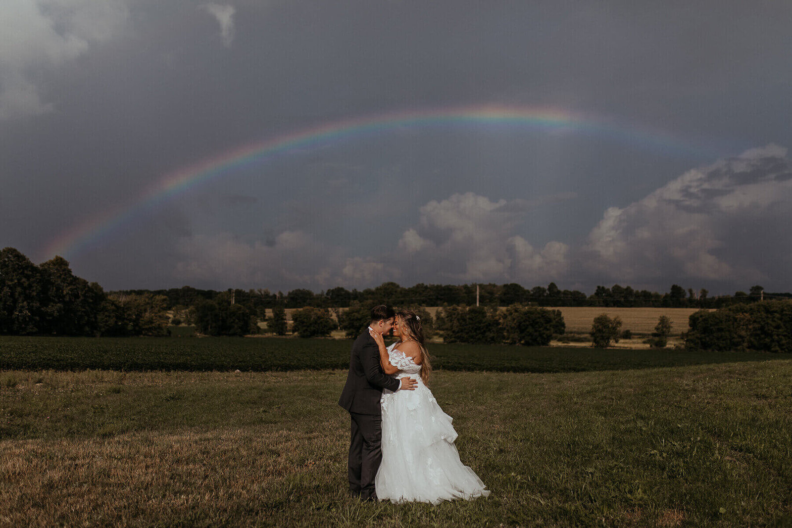 A couple kissing in a field with a rainbow in the background
