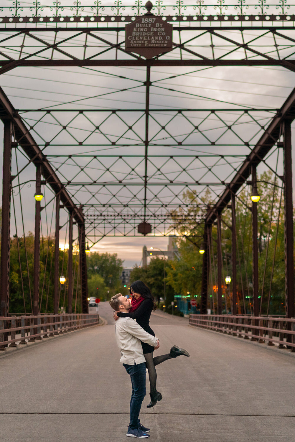 Man lifts woman in black dress on the bridge on Nicollet Island in Minneapolis, Minnesota.