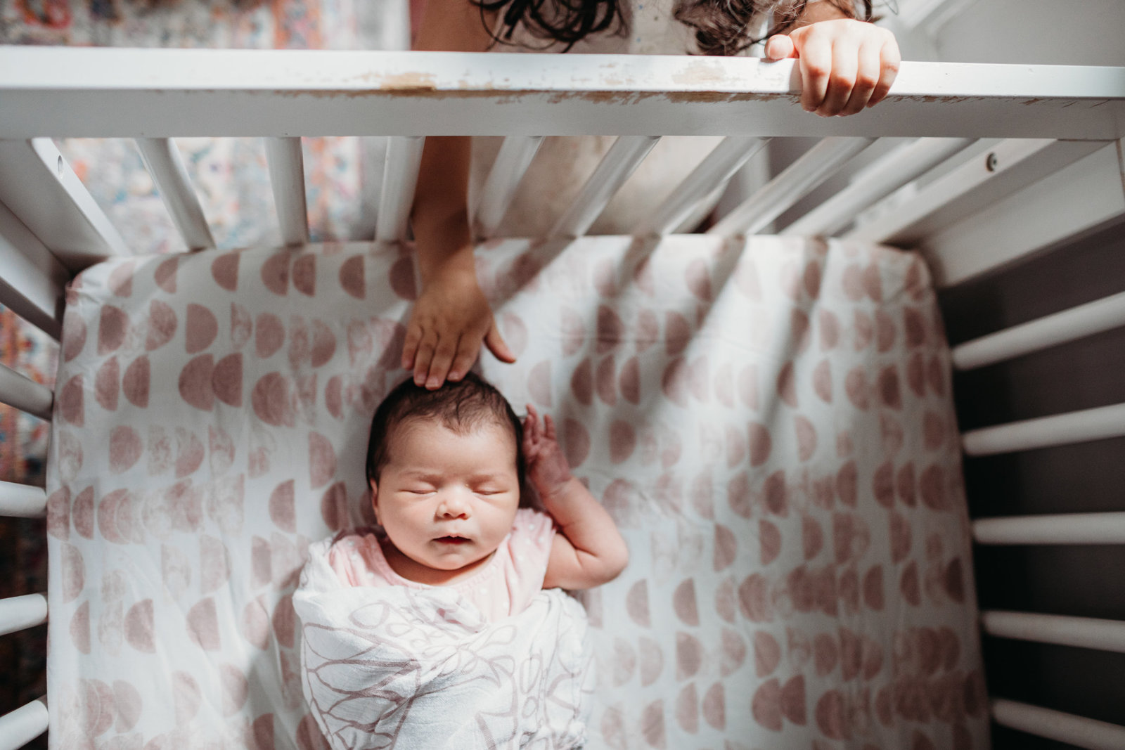 sibling reaches through crib bars to touch babys head during natick newborn session