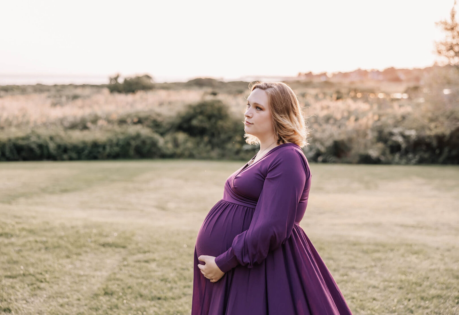 Pregnant woman in purple dress in front of grass field at harkness memorial state park in Waterford, CT