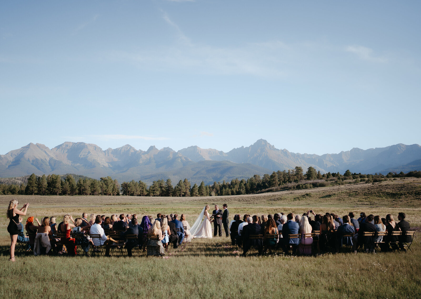 Large summer wedding ceremony with couple and their guests in the field at the Top of the Pines venue in Ouray, Colorado