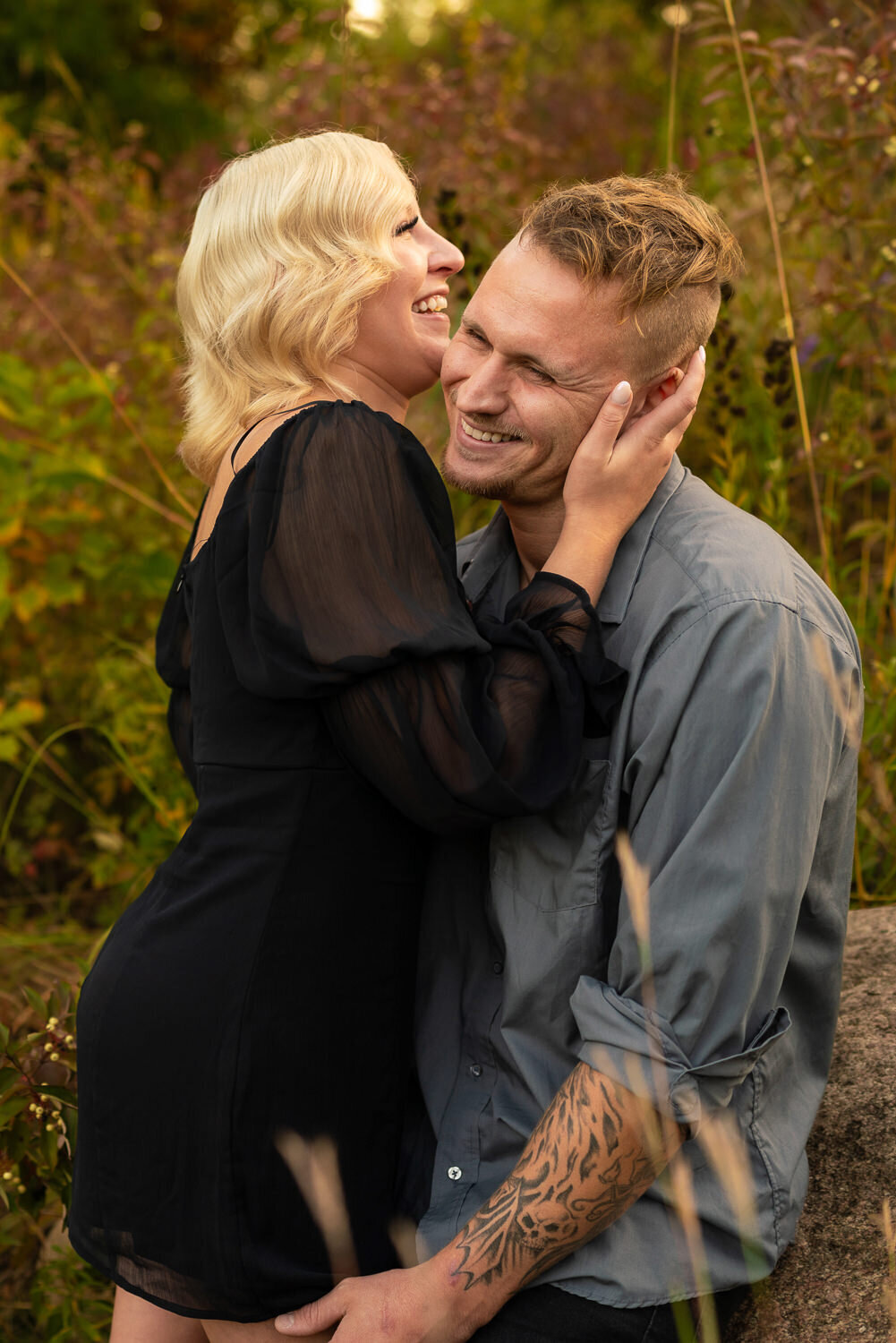 Man and woman in black dress laugh during sunset engagement photography.