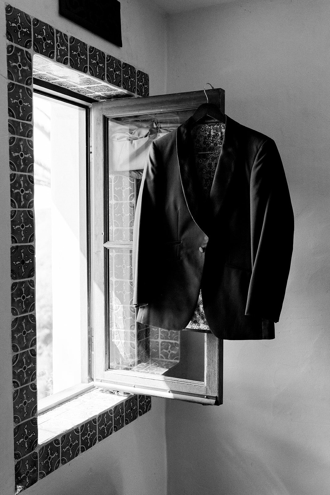 Black and white film image of groom’s suit hanging beside traditional Spanish-style window at Hummingbird Nest Ranch.
