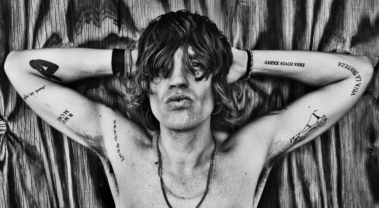 Musician Portrait Nico Stai black and white shirtless arms folded behind his head against wood textured wall