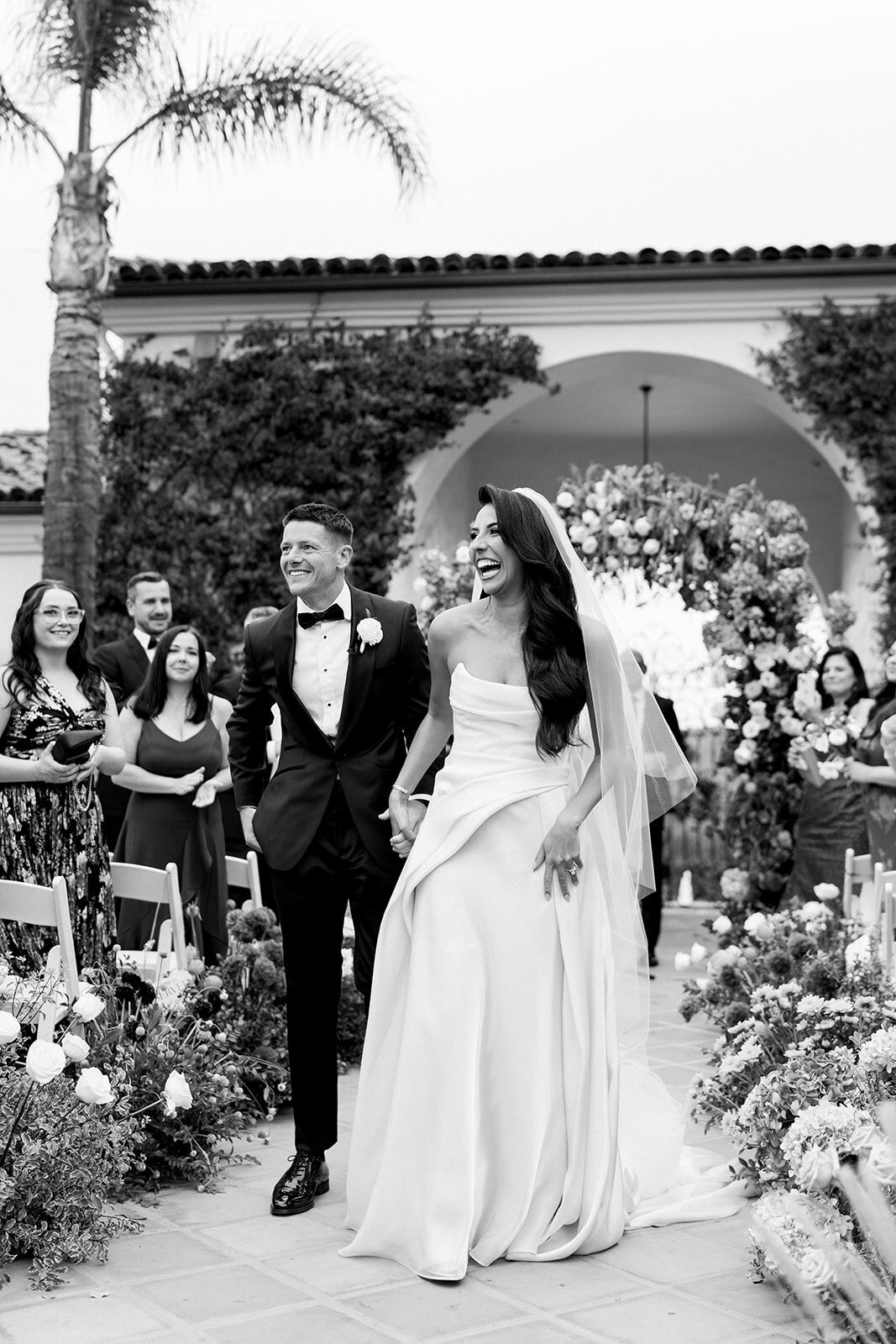 Black and white film image of newlyweds walking back down the aisle after ceremony at Hummingbird Nest Ranch.