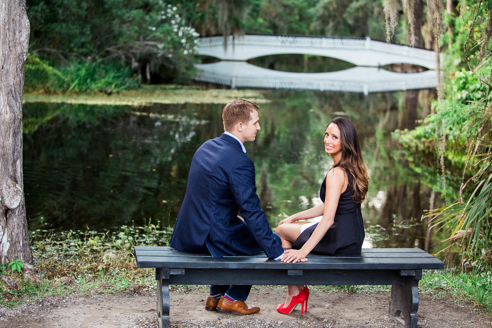 Engaged couple sit on a bench by the white bridge, Magnolia Plantation, Charleston Engagement Photographer.