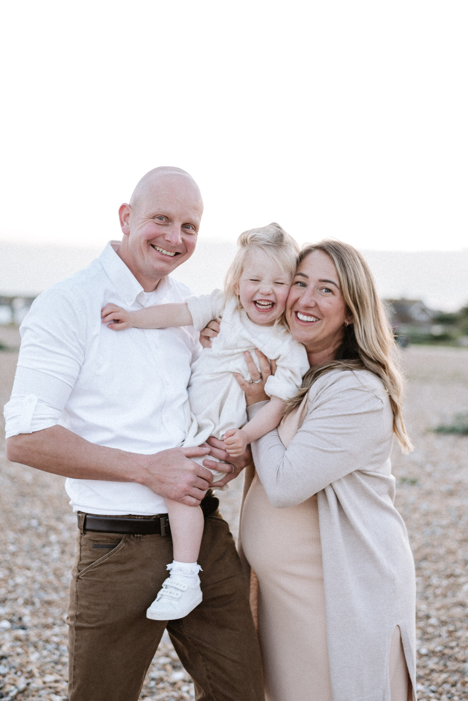 Mother and father holding their daughter smiling at family photoshoot on the beach in west sussex