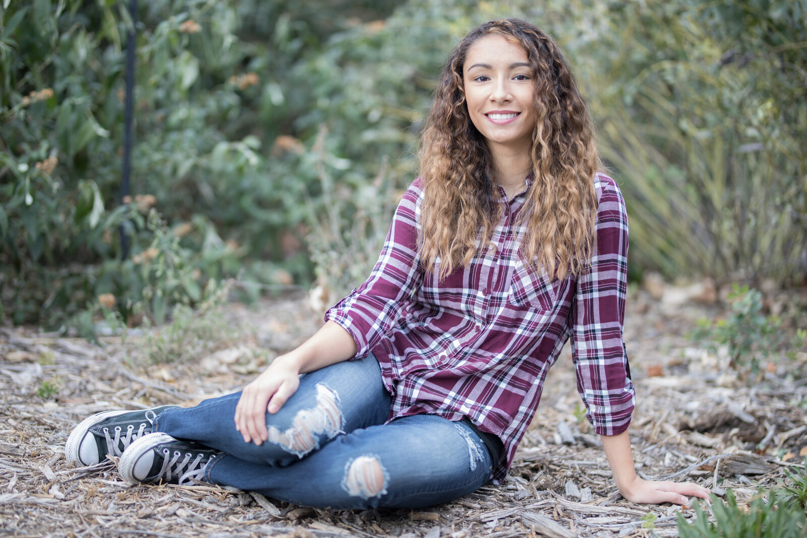 Sitting on the ground in a plaid shirt during a senior photo shoot