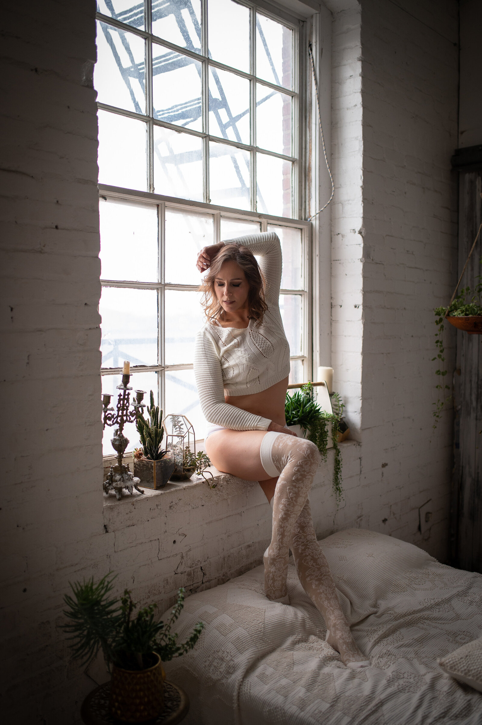 woman wearing white sweater and lace stockings sitting in window with arm up over her head