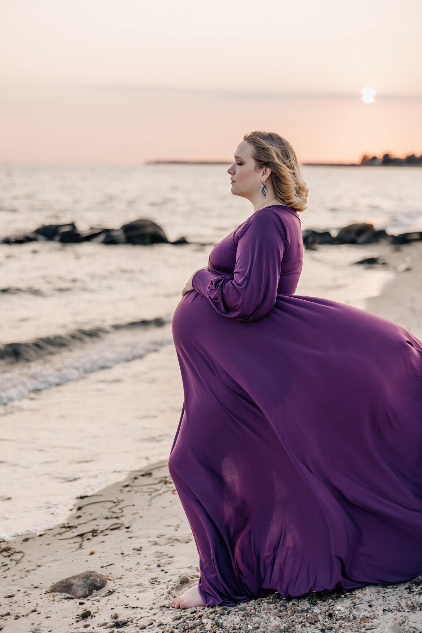 Pregnant woman on beach at sunset in purple dress