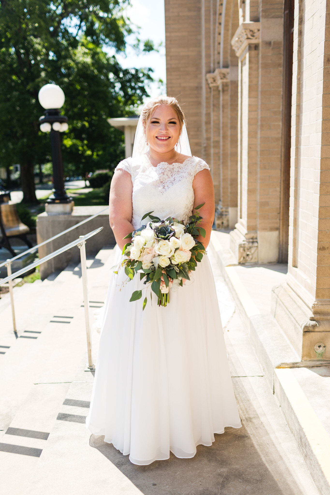 bride smiling outside of church for portrait with veil and flowers ohio 