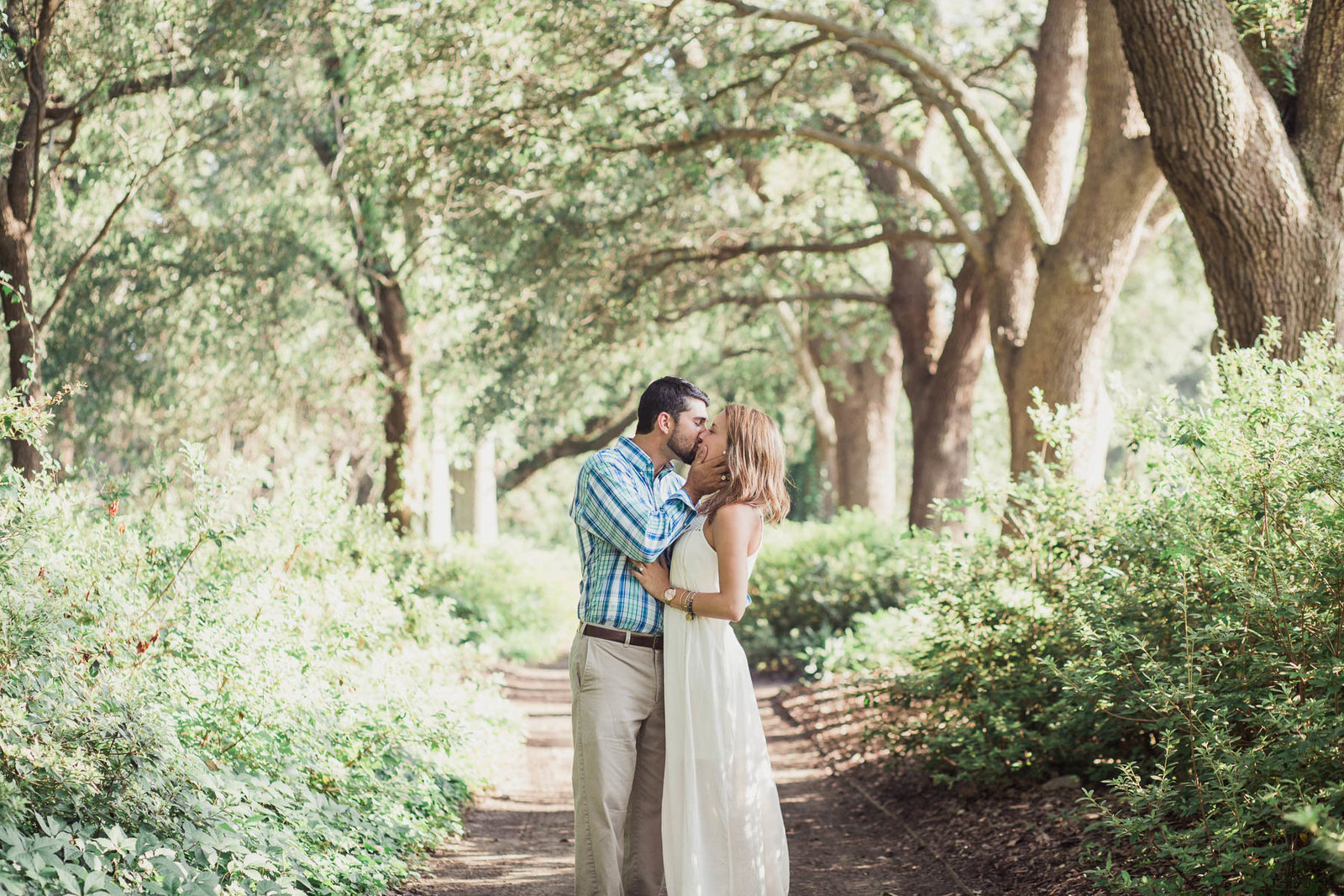 Engaged couple stand in path of oak trees, Hampton Park, Charleston, South Carolina