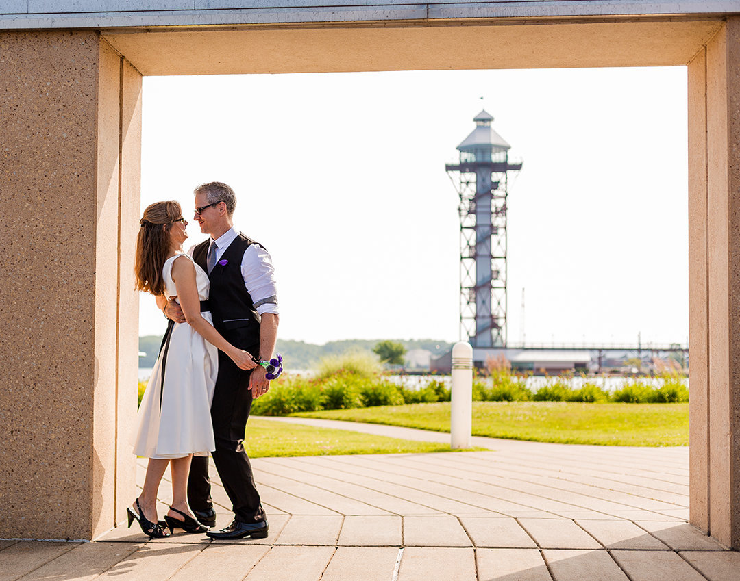 Bride and groom embrace in alcove with Bicentennial Tower in the background