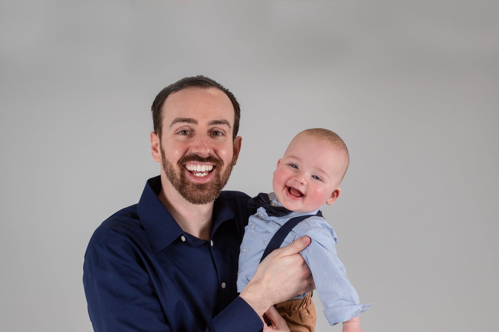 Father in son in Boxborough studio smiling at camera on a gray background
