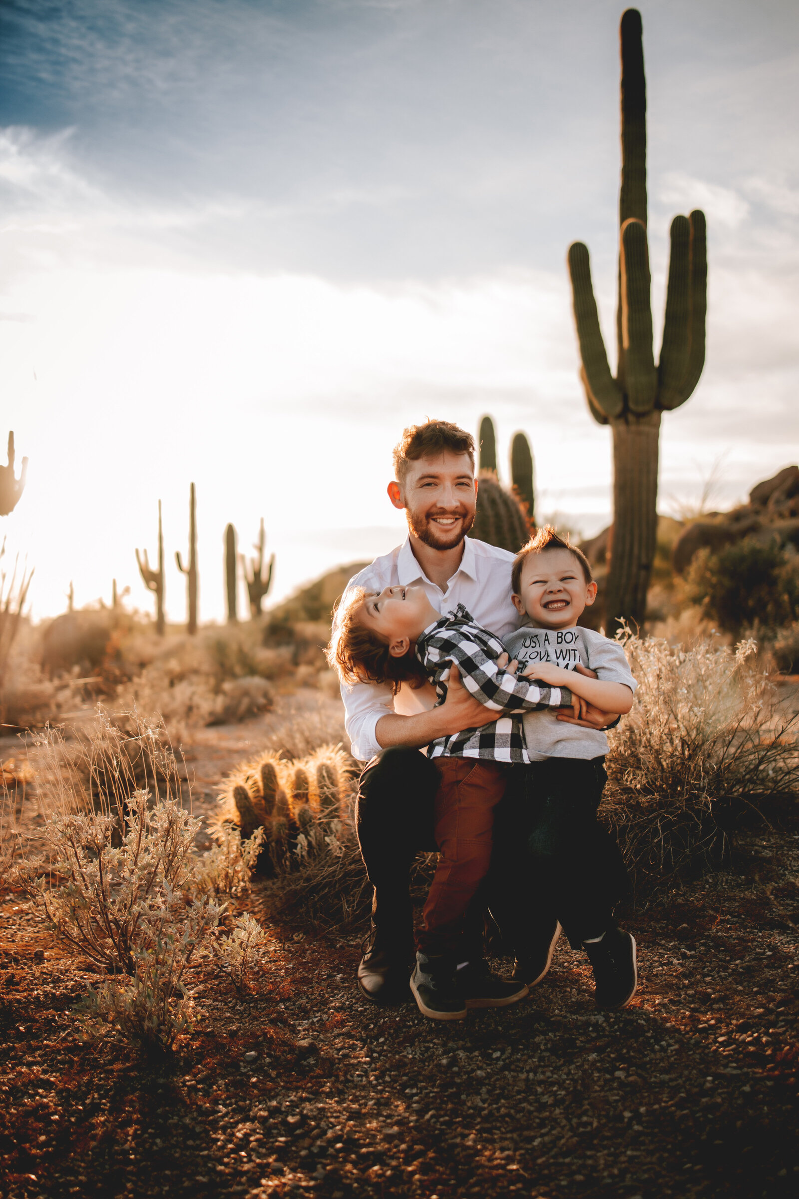 dad holds two young boys in arizona with one large cactus behind him