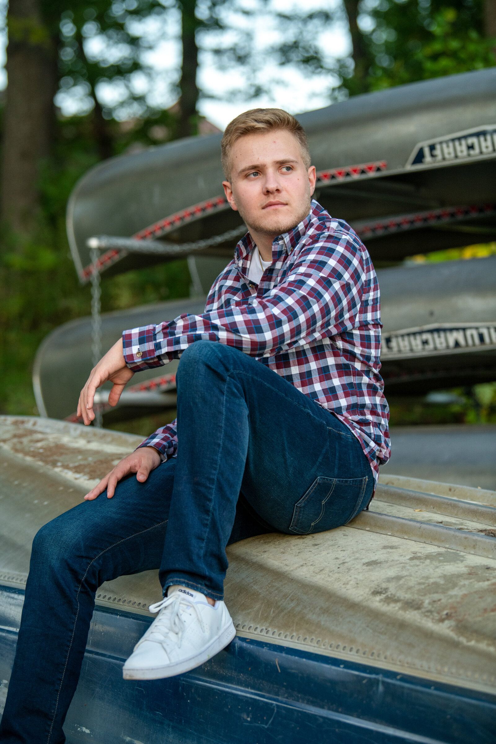Lino Lakes Minnesota high school senior boy wearing plaid and sitting on a canoe in nature