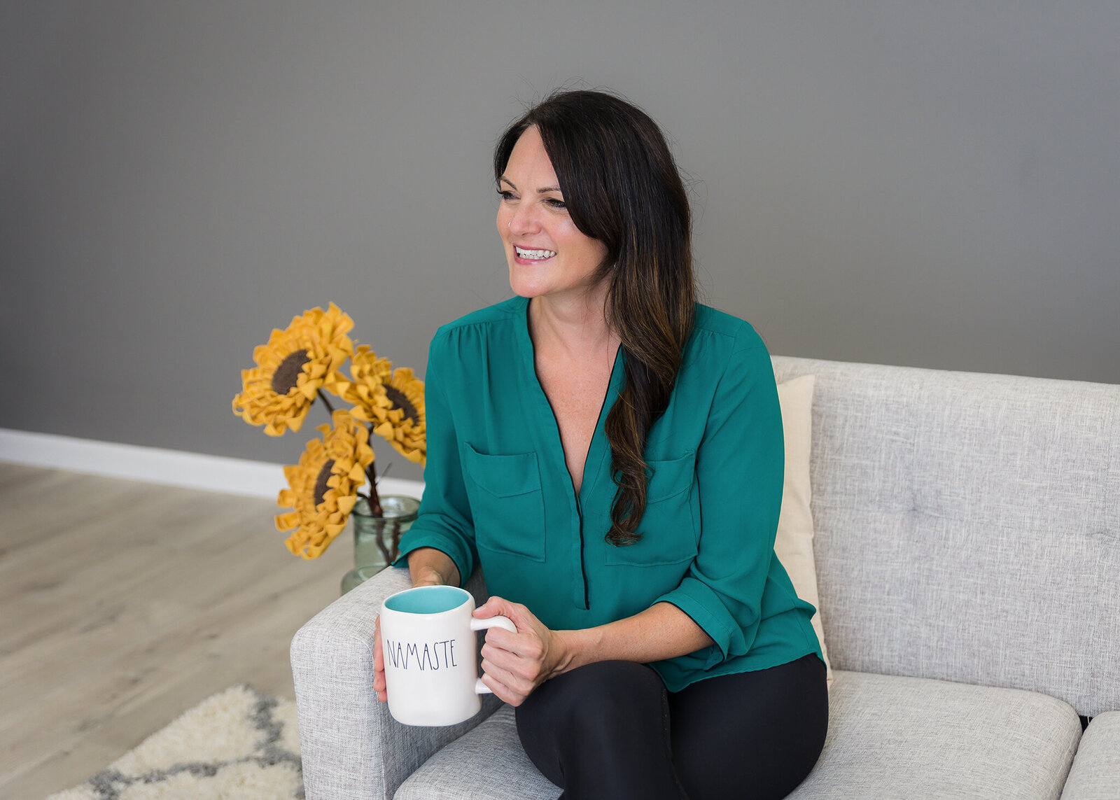 woman sitting on the couch with a cup of coffee looking to the side smiling