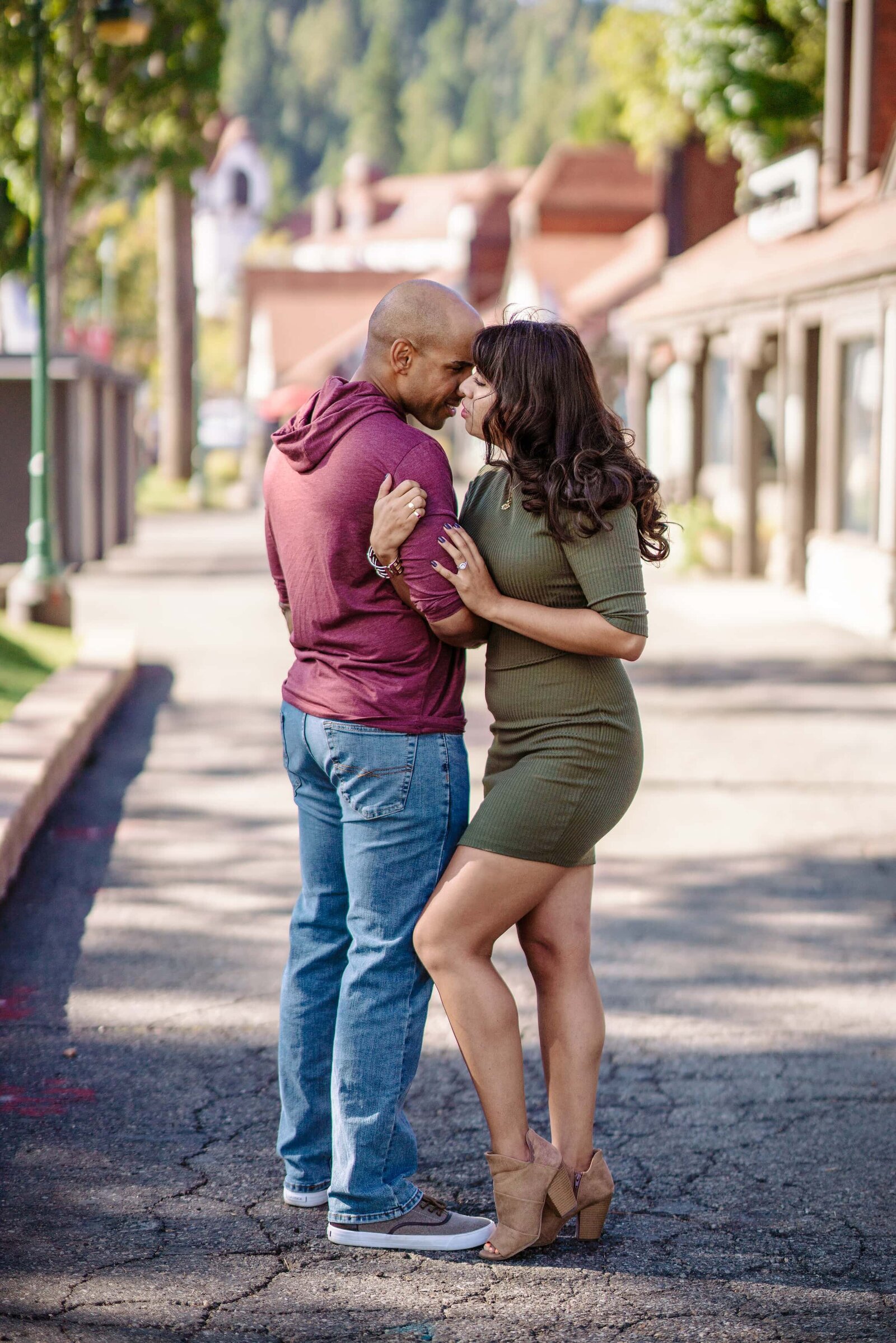 Man in jeans and mauve shirt hugging girl in green dress posing in Village of Lake Arrowhead.