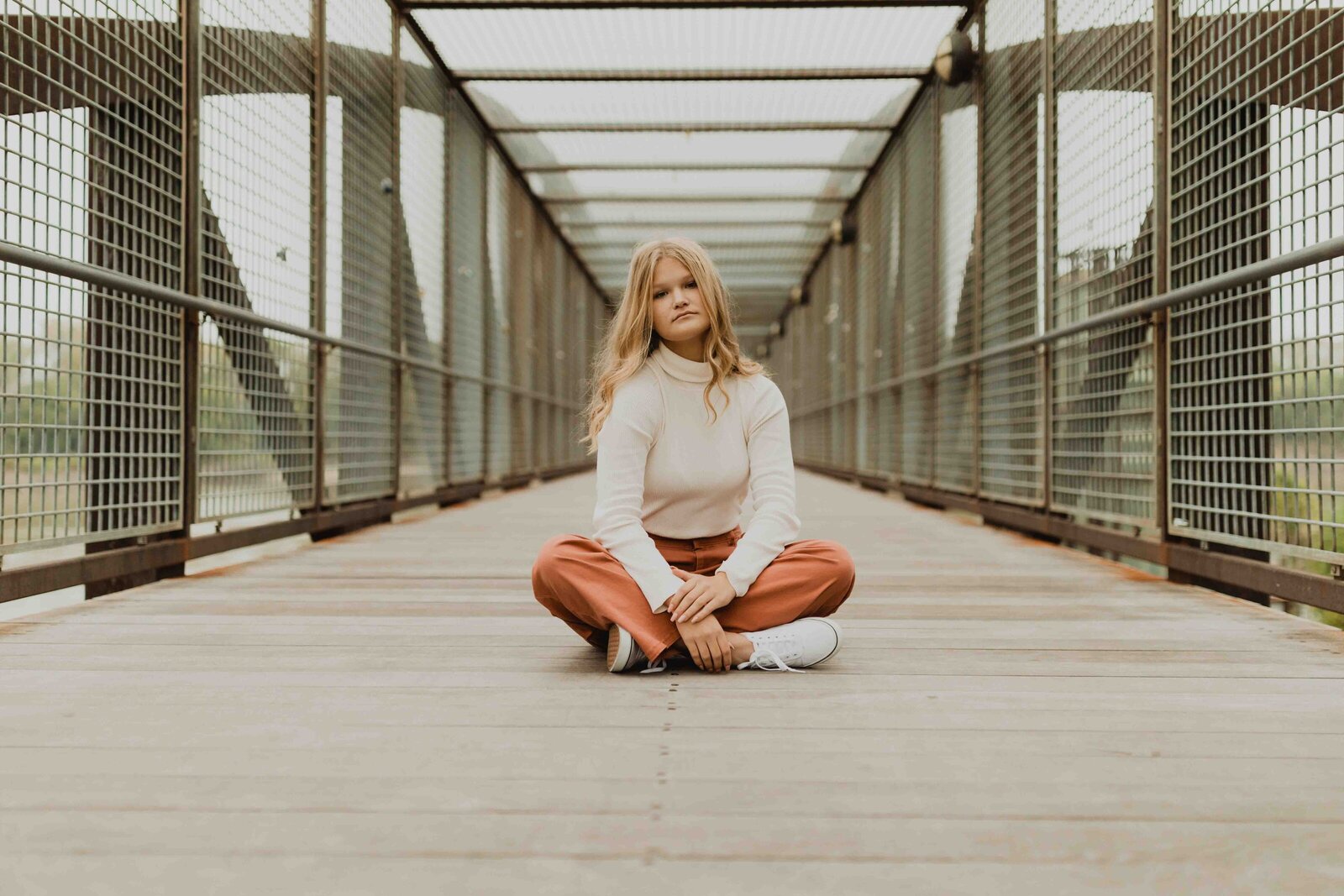 Senior girl sitting in the middle of walking bridge, legs crossed and looking straight into camera.