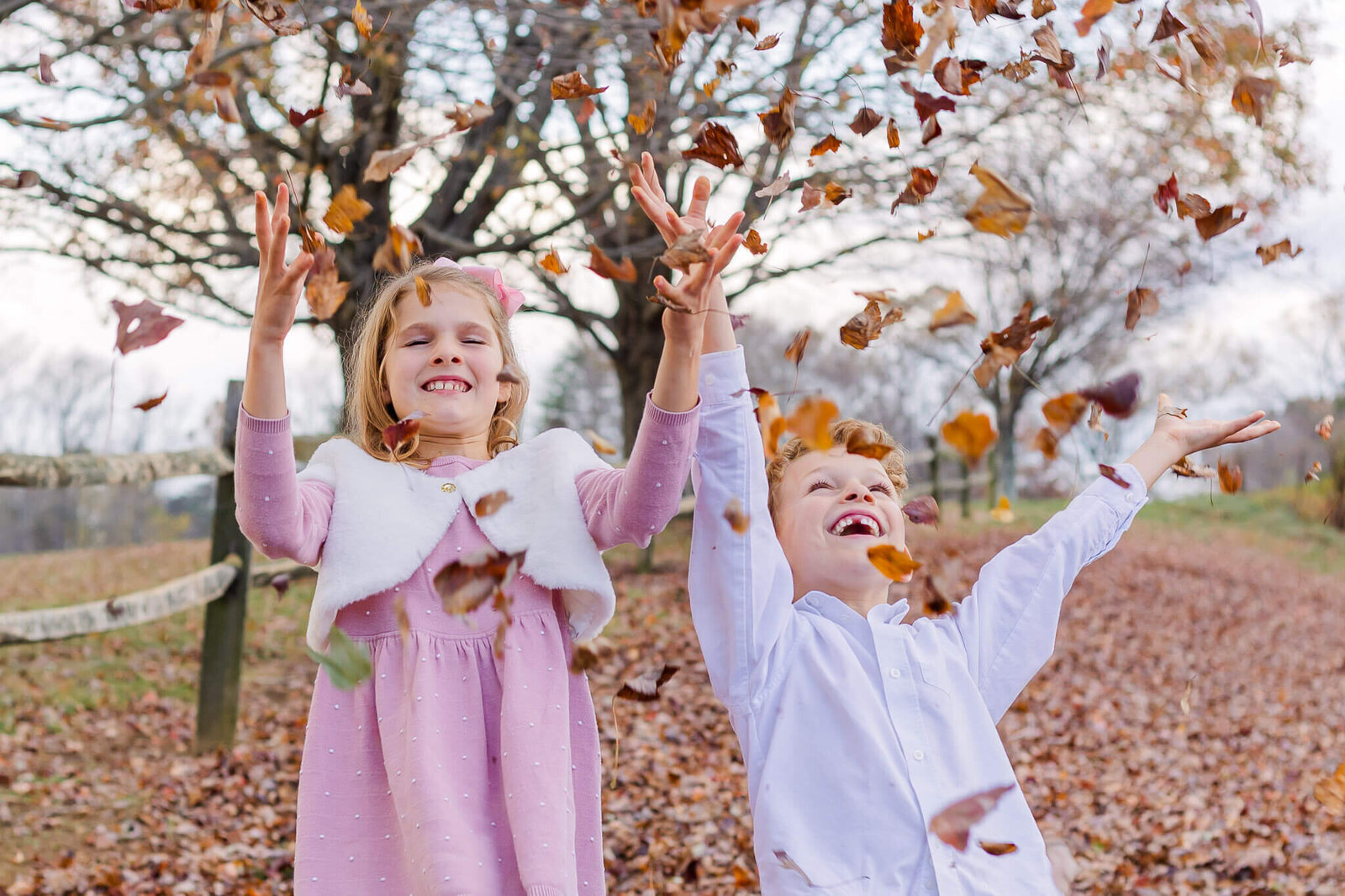 A brother and sister tossing leaves in the air.