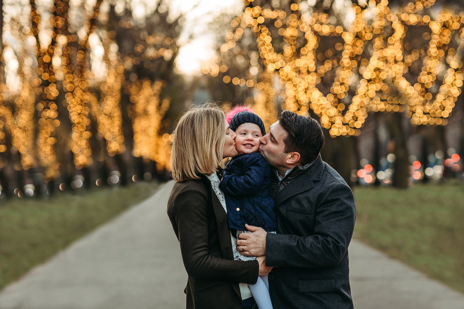 parents snuggle toddler outdoors by christmas lights in winter family session in boston