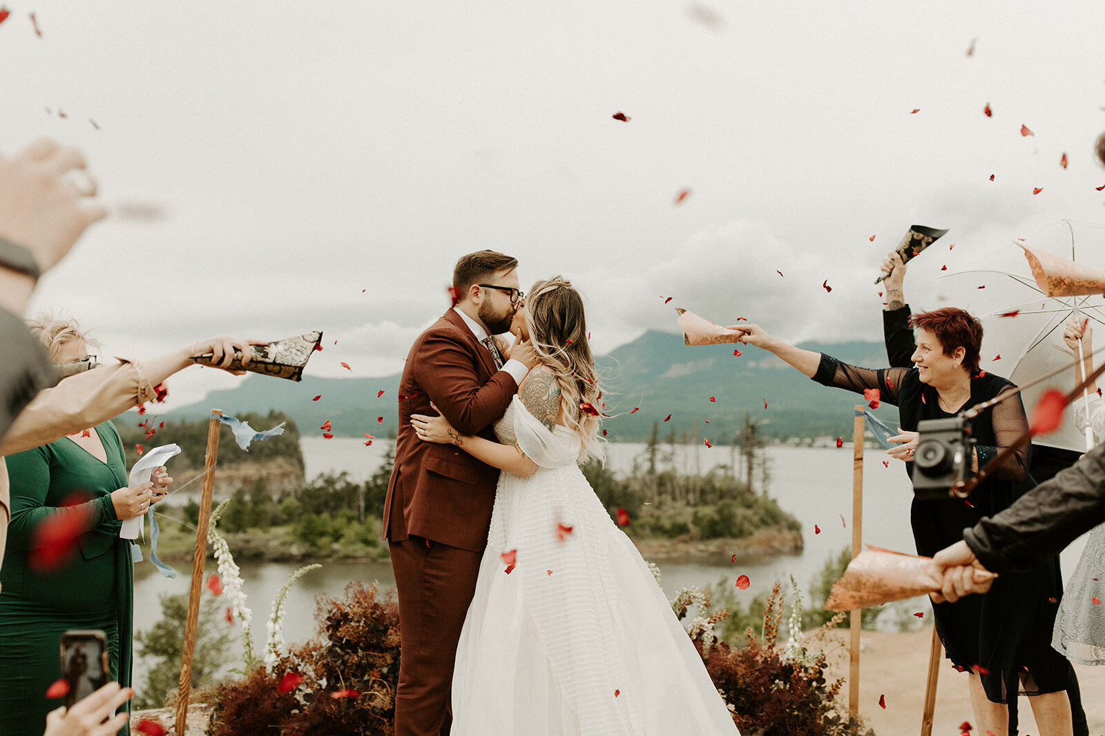 bride and groom first kiss as rose petals are thrown over them