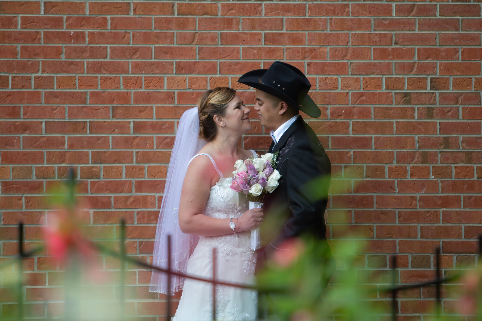 Bride and groom about to kiss in front of brick wall at Fort Edmonton Park