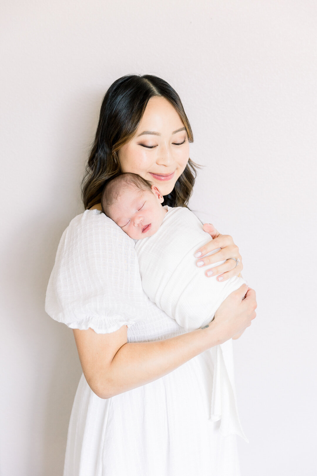 Image of mother holding newborn baby in white wrap taken by Sacramento Newborn Photographer Kelsey krall