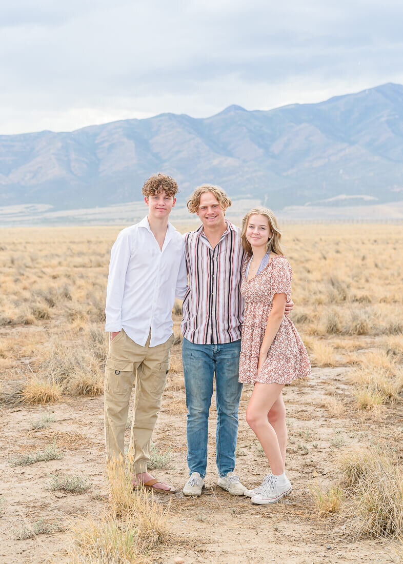 A teenage girl and her two teenage brothers have their arms around each other while standing in a field in Eagle Mountain.