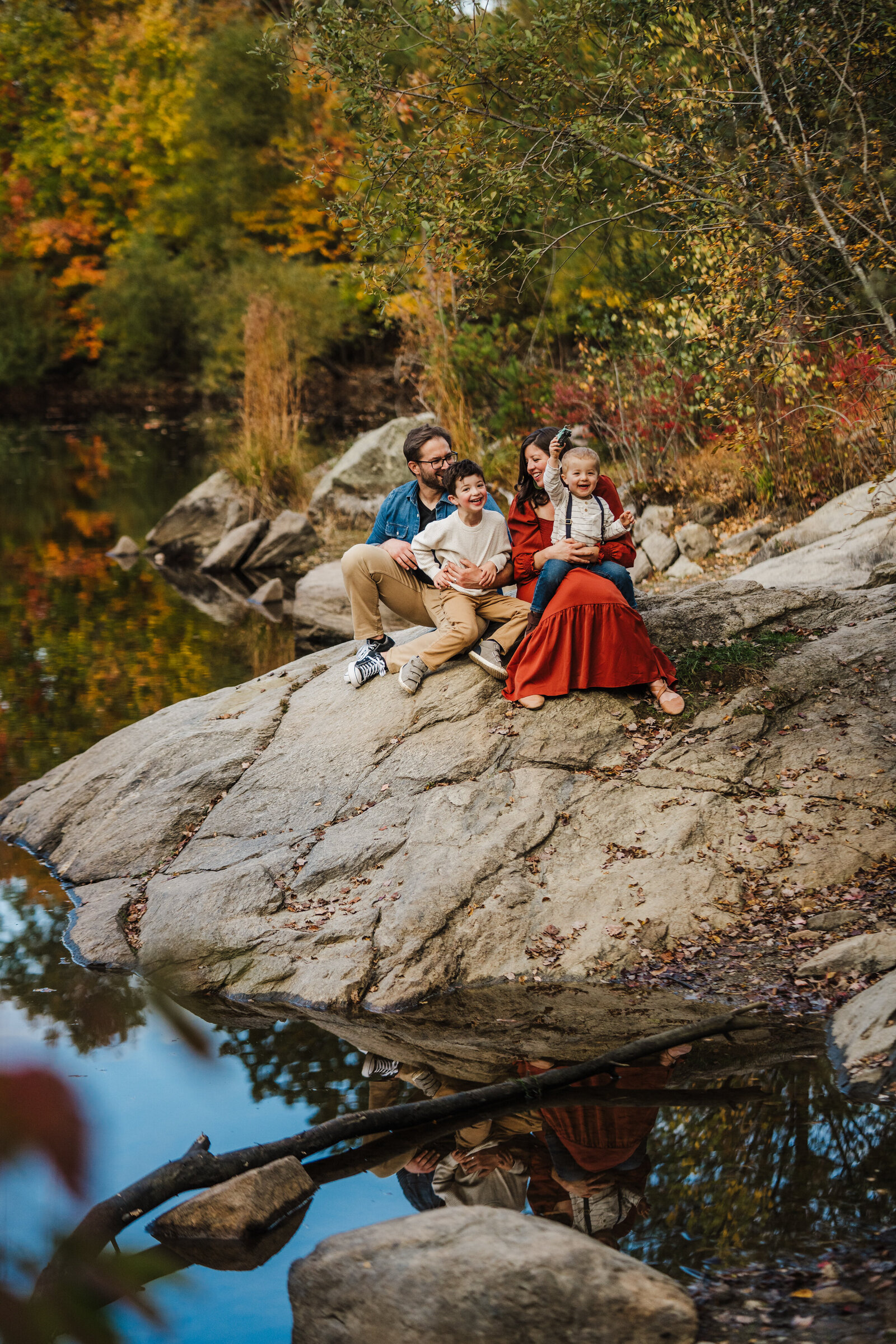 family laughs on a rock in a pond in autumn