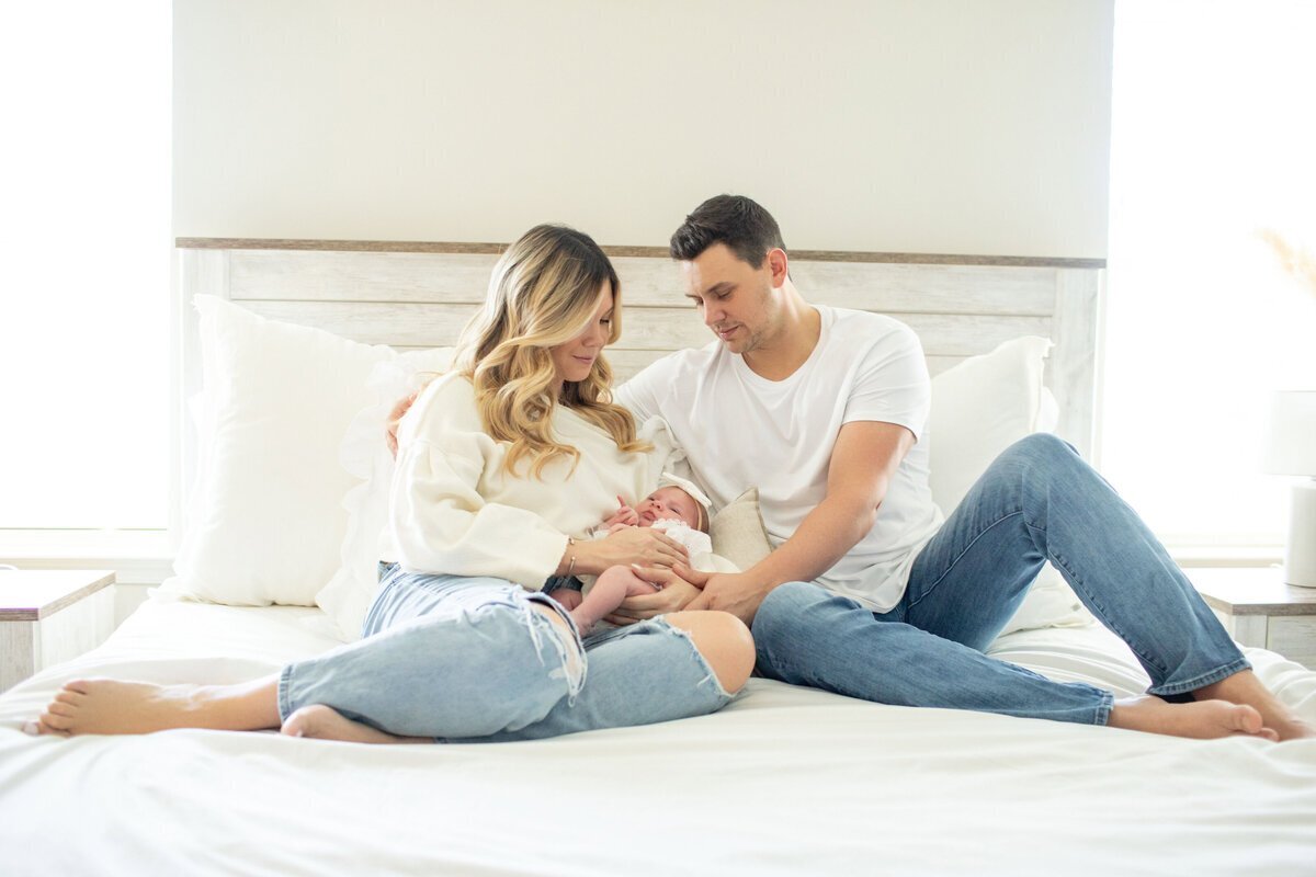 Parents looking at newborn baby while sitting on bed, taken by newborn photography in new jersey