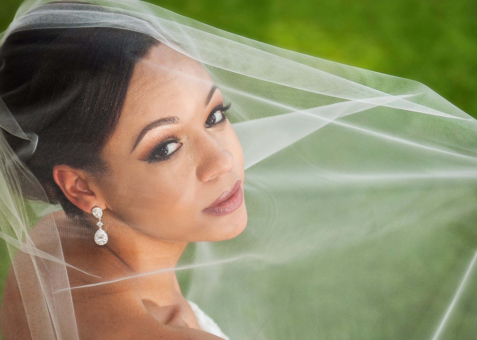 Gorgeous black bride headshot with her veil over her face wearing diamond earrings in San Antonio