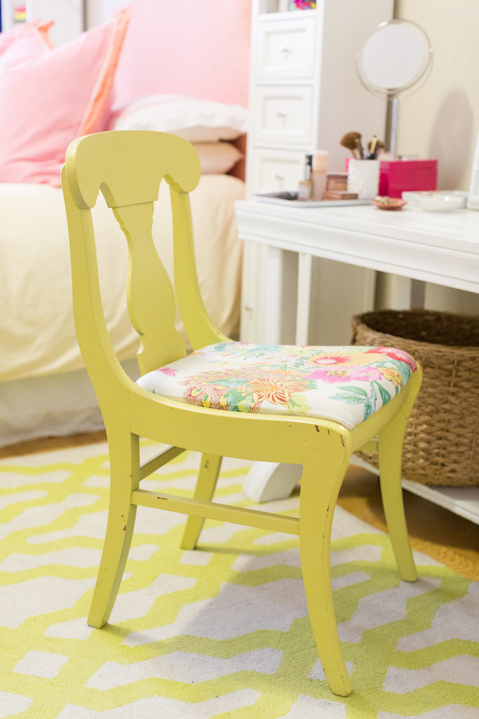 A yellow chair with flower upholstery in front of a vanity.