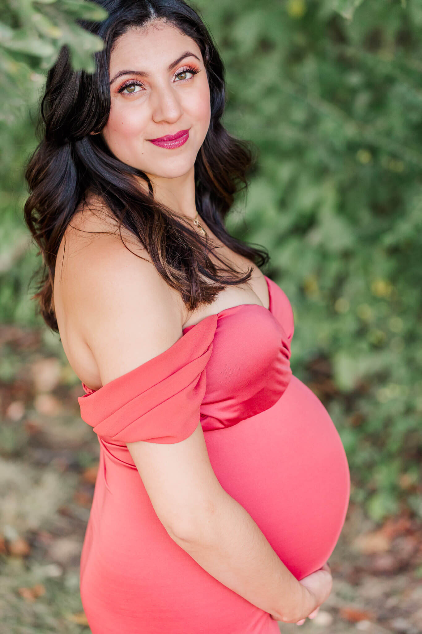 An outdoor Woodbridge maternity portrait session of a pregnant woman wearing a pink dress.