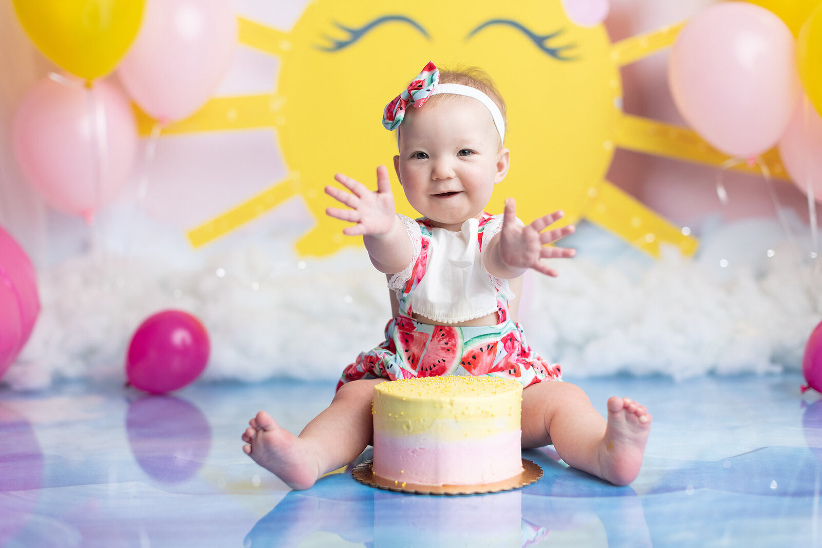 Girl holds out hands at summer themed cake smash.