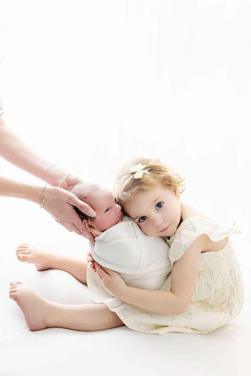 Little girl sibling holding newborn baby, with mom's arms supporting, taken by best newborn photographers nj
