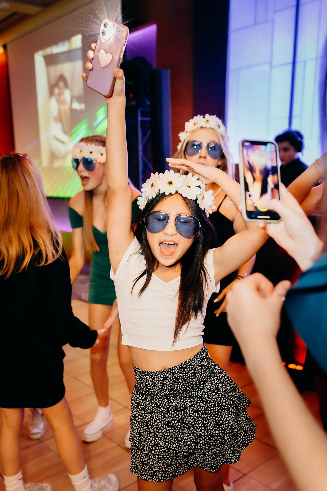 A teem girl in a skirt and white shirt dances in blue sunglasses and flower headband on the dance floor for Bellevue Bar and Bat Mitzvah Photography