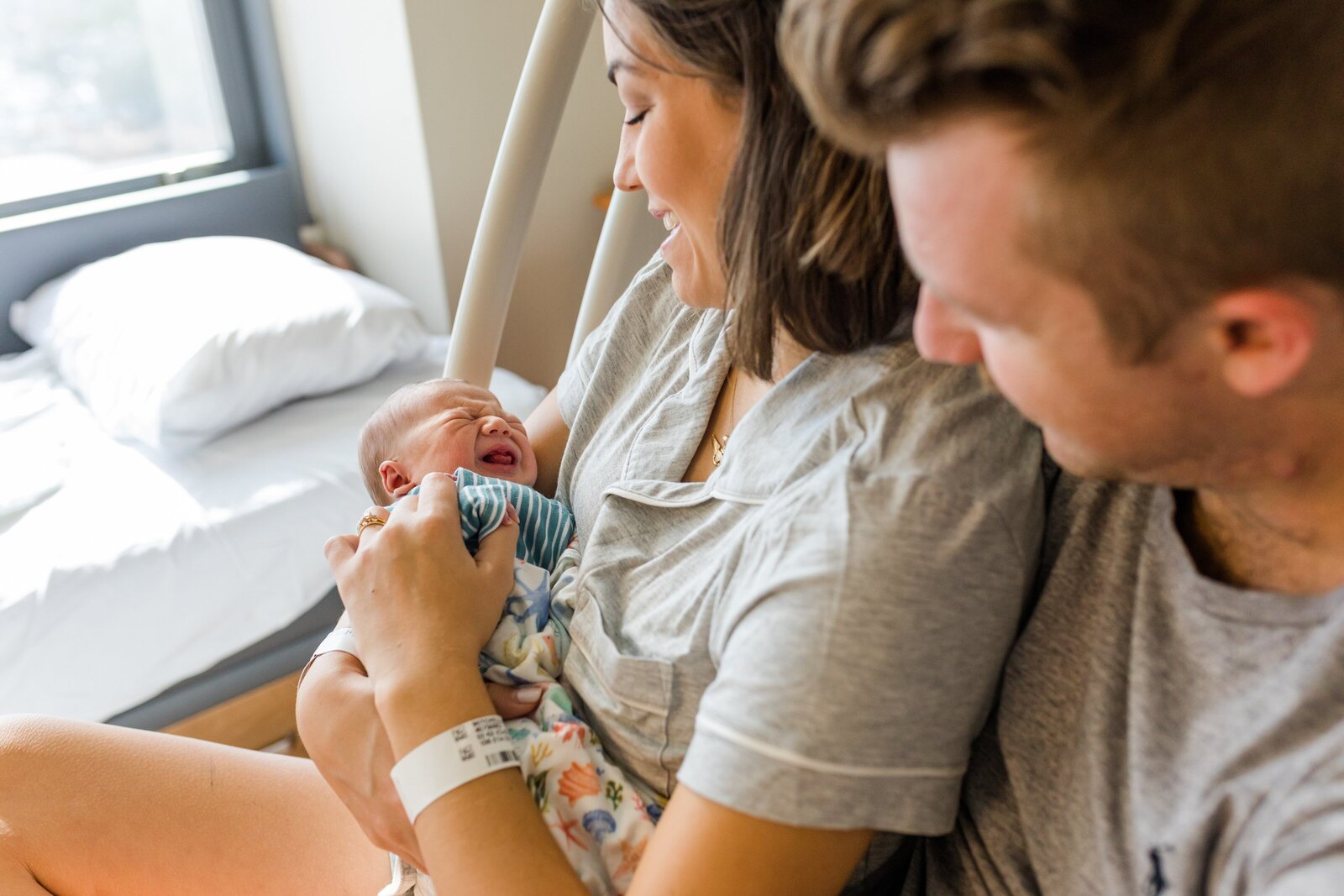 Mom and dad holding newborn in hospital bed during fresh 48 newborn  photos.  Newborn son is wearing Copper Pearl brand Nautical swaddle.