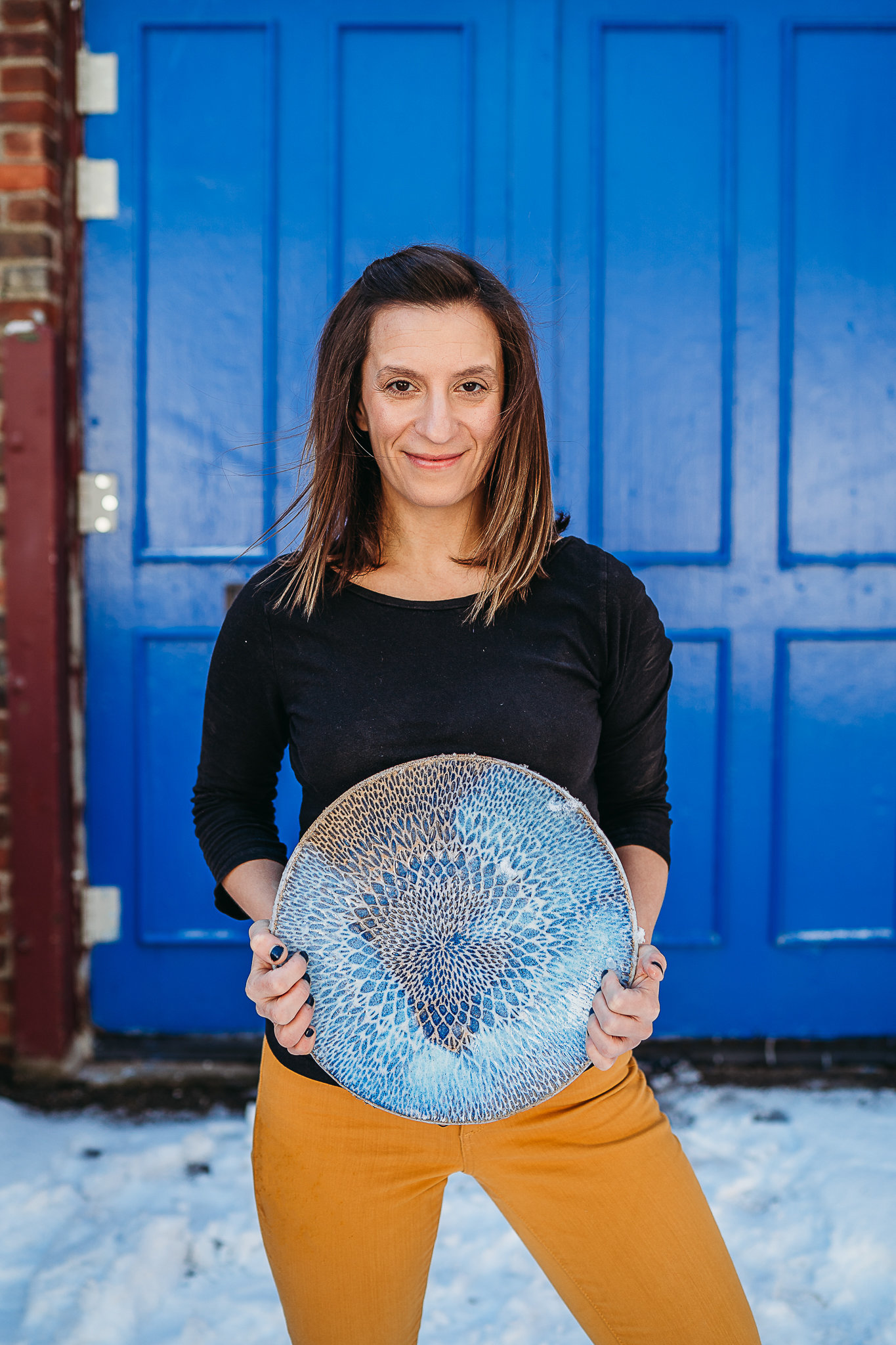 female potter holds platter in front of bright blue door