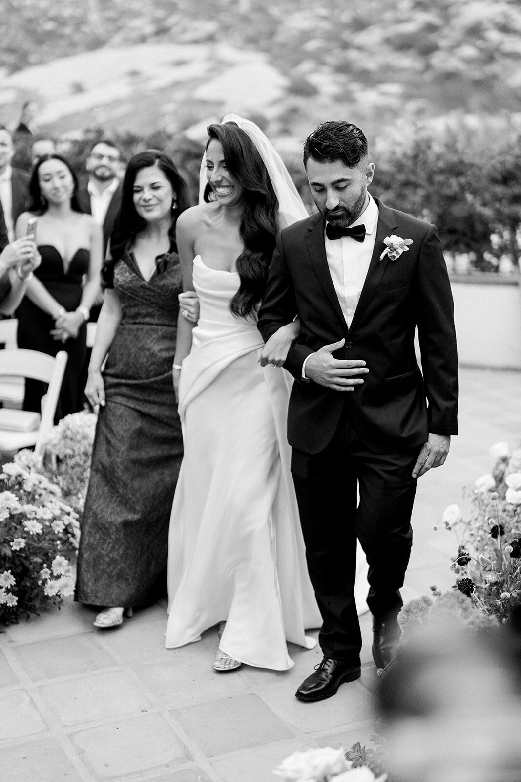 Bride and groom walk hand in hand with wedding party trailing behind, captured in luxury documentary style at Hummingbird Nest Ranch.