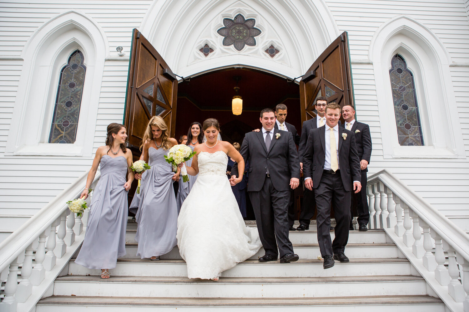 bride and groom and wedding party coming out of church doors