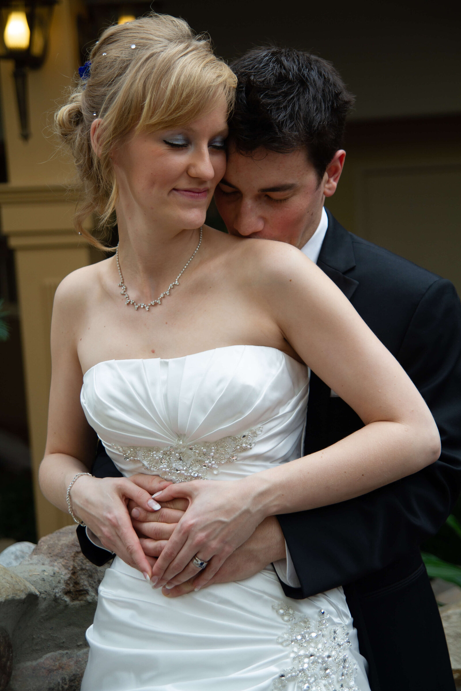 Groom holding bride from behind, kissing her gently on the neck