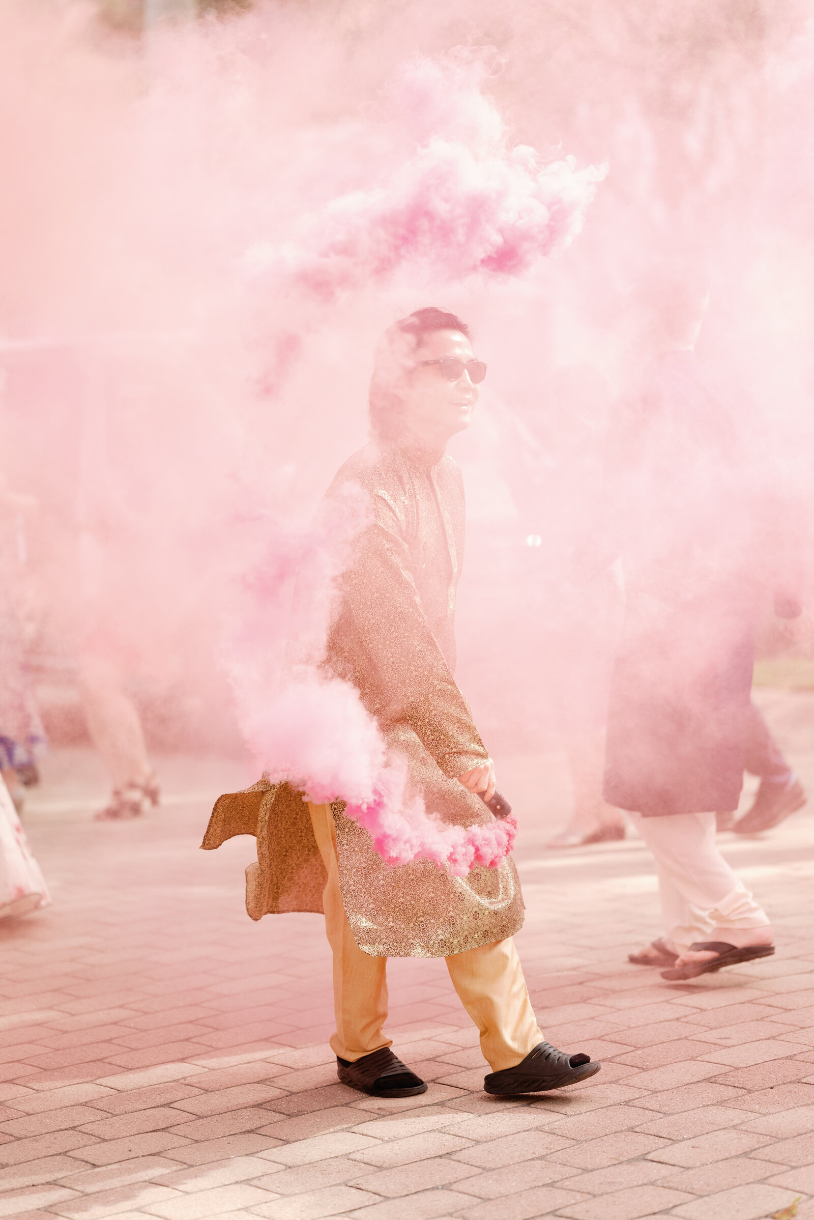 Groomsman  engulfed in pink smoke bomb during the wedding day baraat