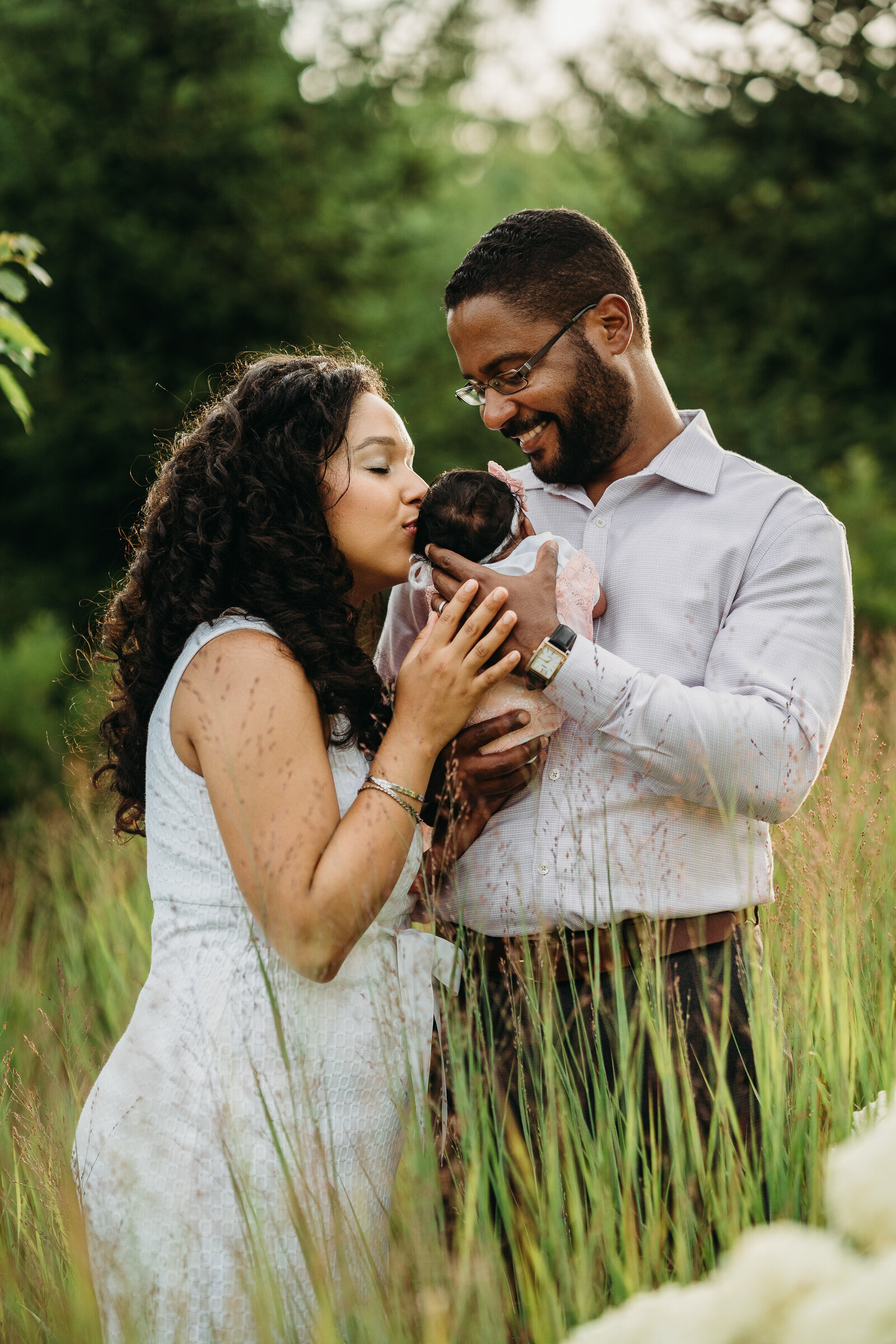 couple kisses newborn while standing in long grass