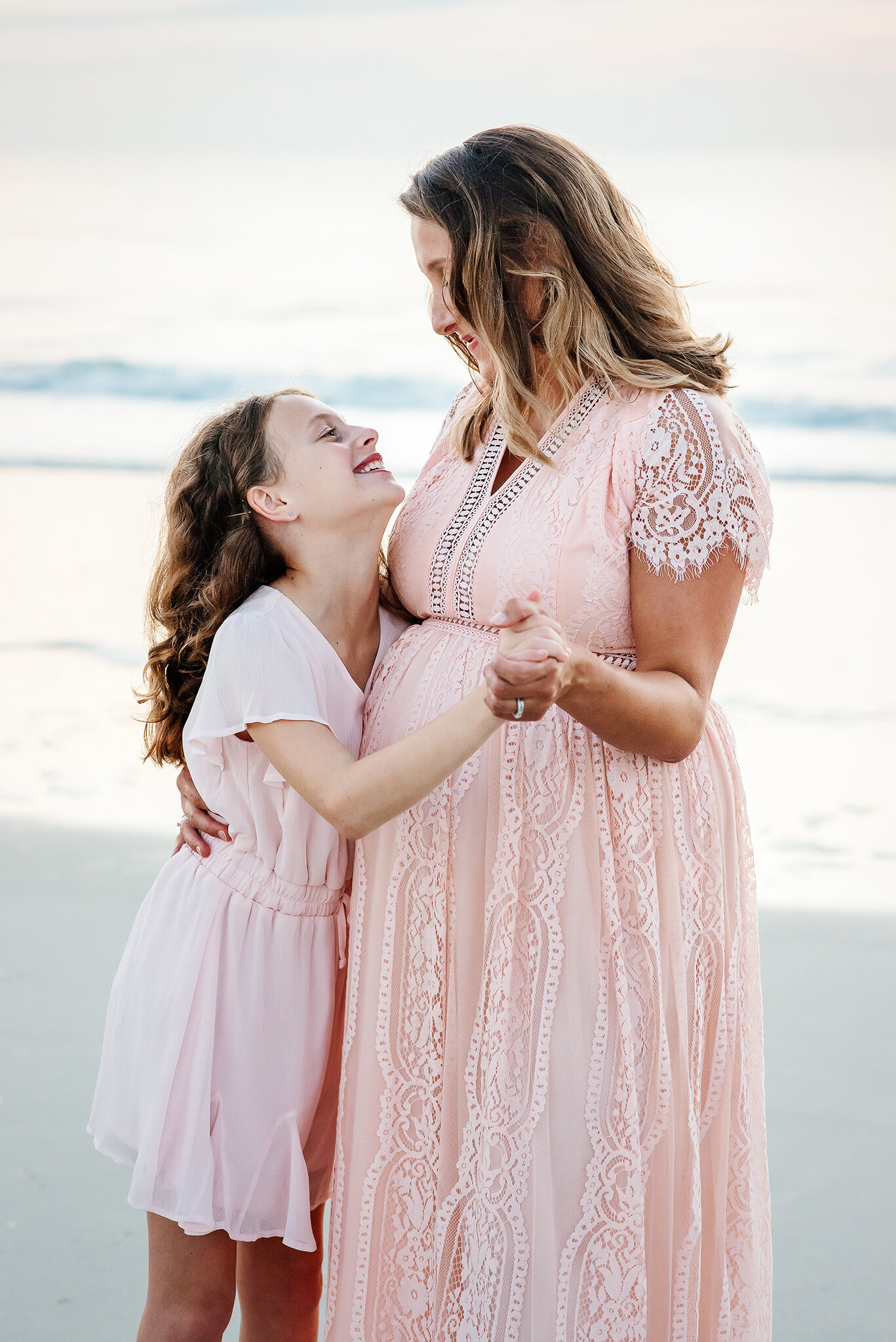 Expectant mom and daughter in pink dresses dance at Atlantic Beach, FL.