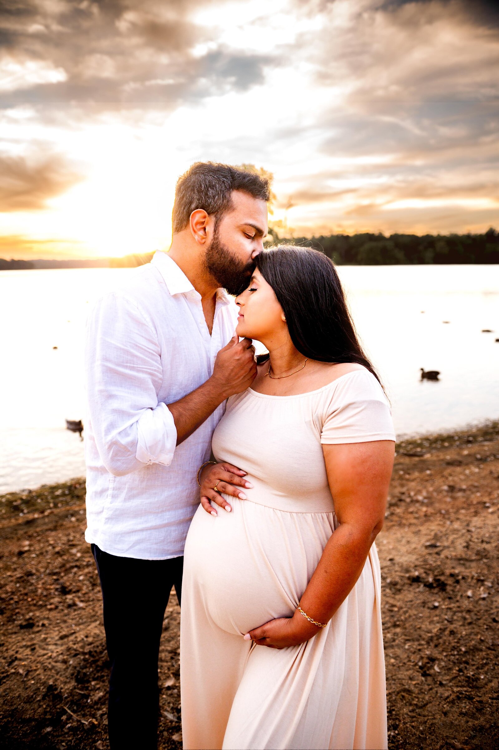 husband kissing pregnant wife while holding her chin