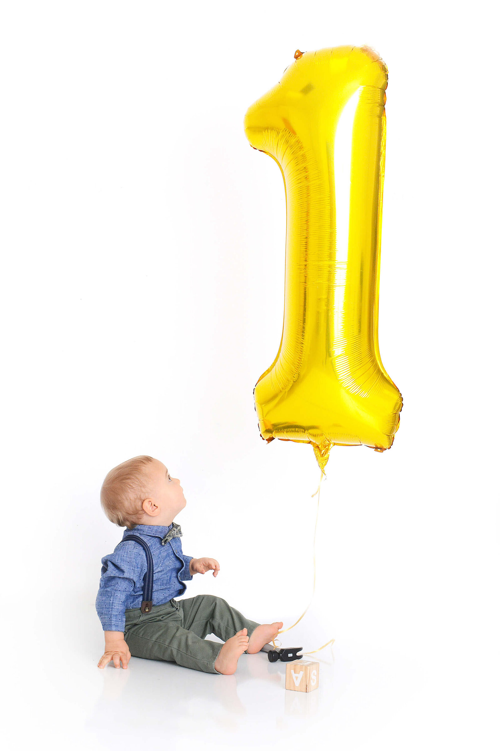 boy smiles up at a 1 shaped balloon at his first birthday photoshoot